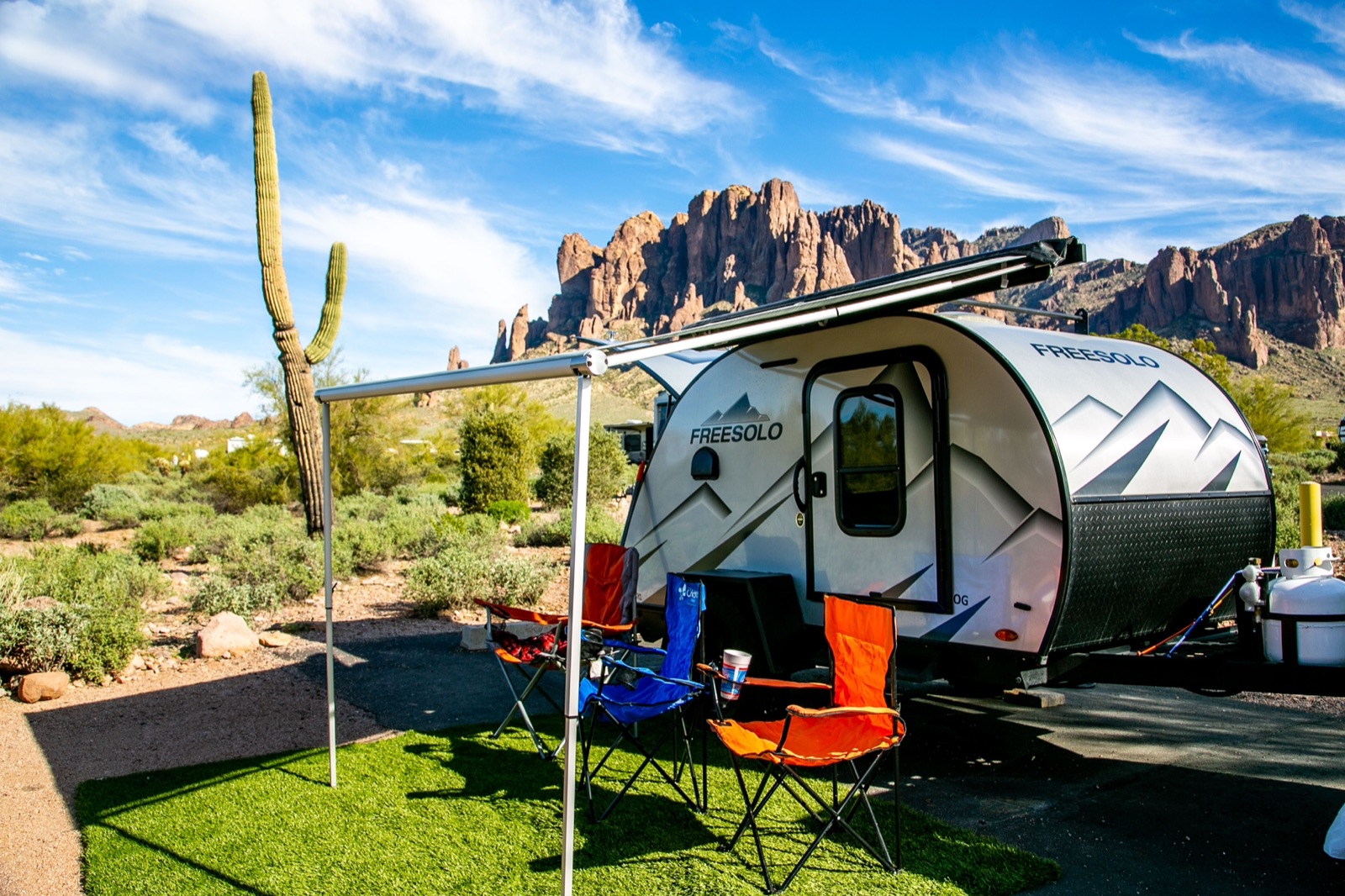 A small teardrop camper with camp chairs below the Superstition Mountains and a saguaro near Apache Junction