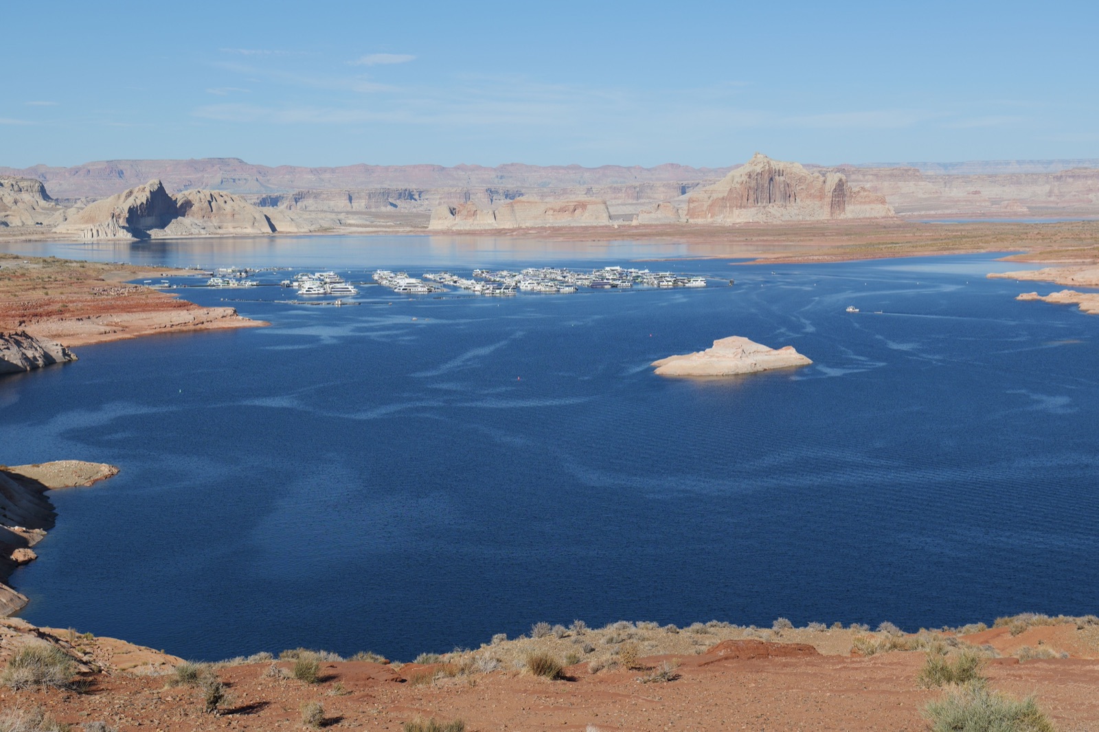 Blue water of Lake Powell among red rock shores, with houseboats moored in a bay