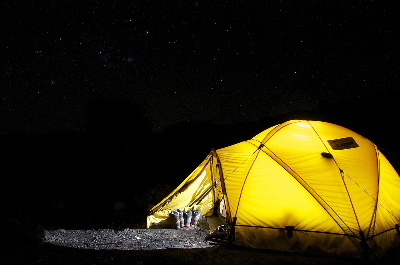 A yellow dome tent lit from inside under a dark, starry night sky