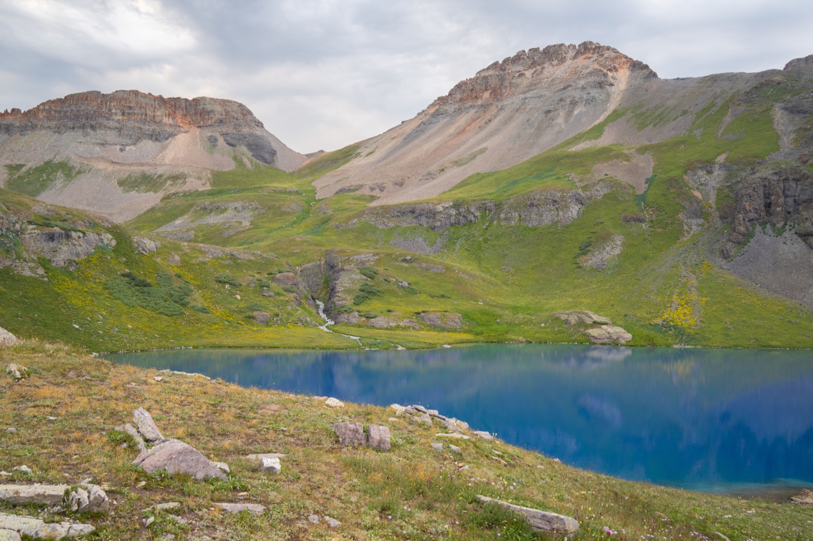A deep blue alpine lake below rocky peaks and green slopes in the San Juan National Forest