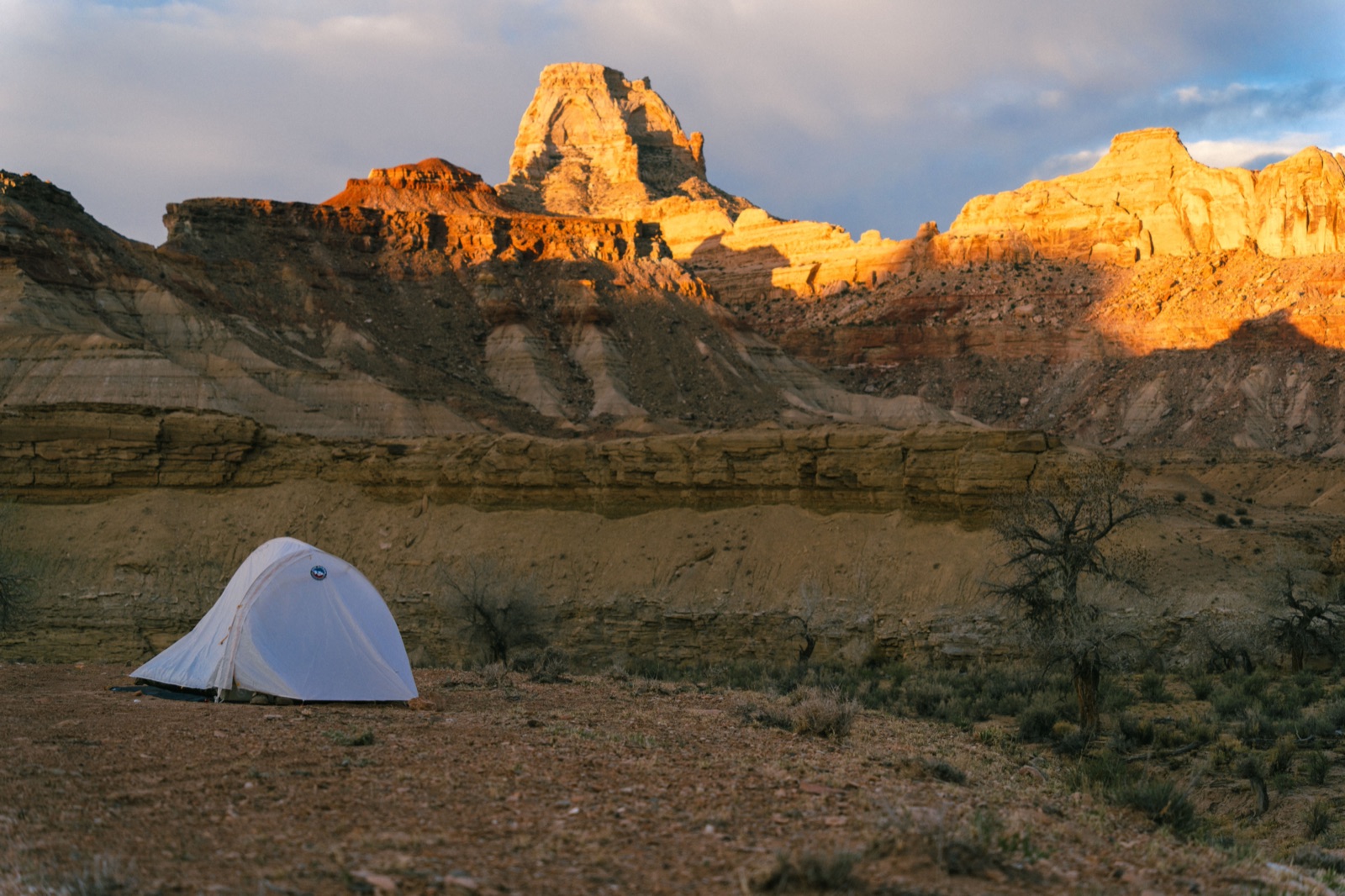 A single tent on open desert ground below sunlit sandstone buttes in Utah