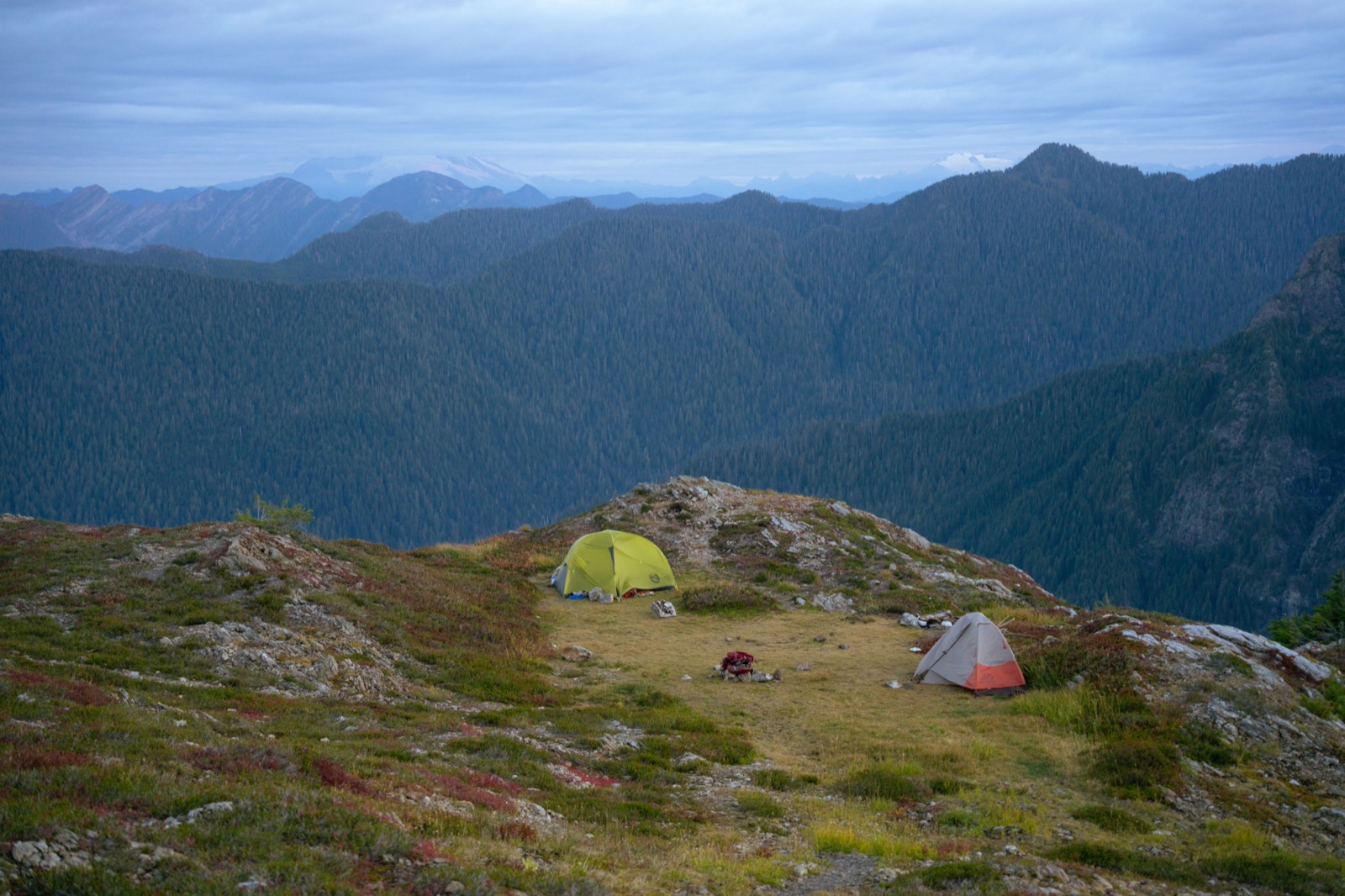 Two tents on a grassy, rocky ridge at Goat Flats, above forested Cascade valleys in Washington