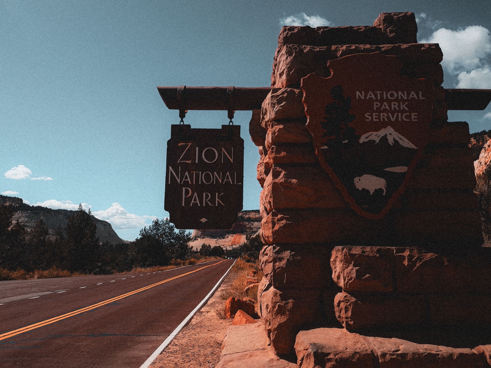 The Zion National Park entrance sign on a red sandstone wall beside the park road