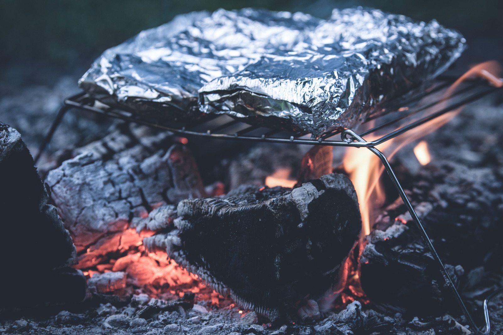 A foil packet on a wire grate over glowing campfire coals