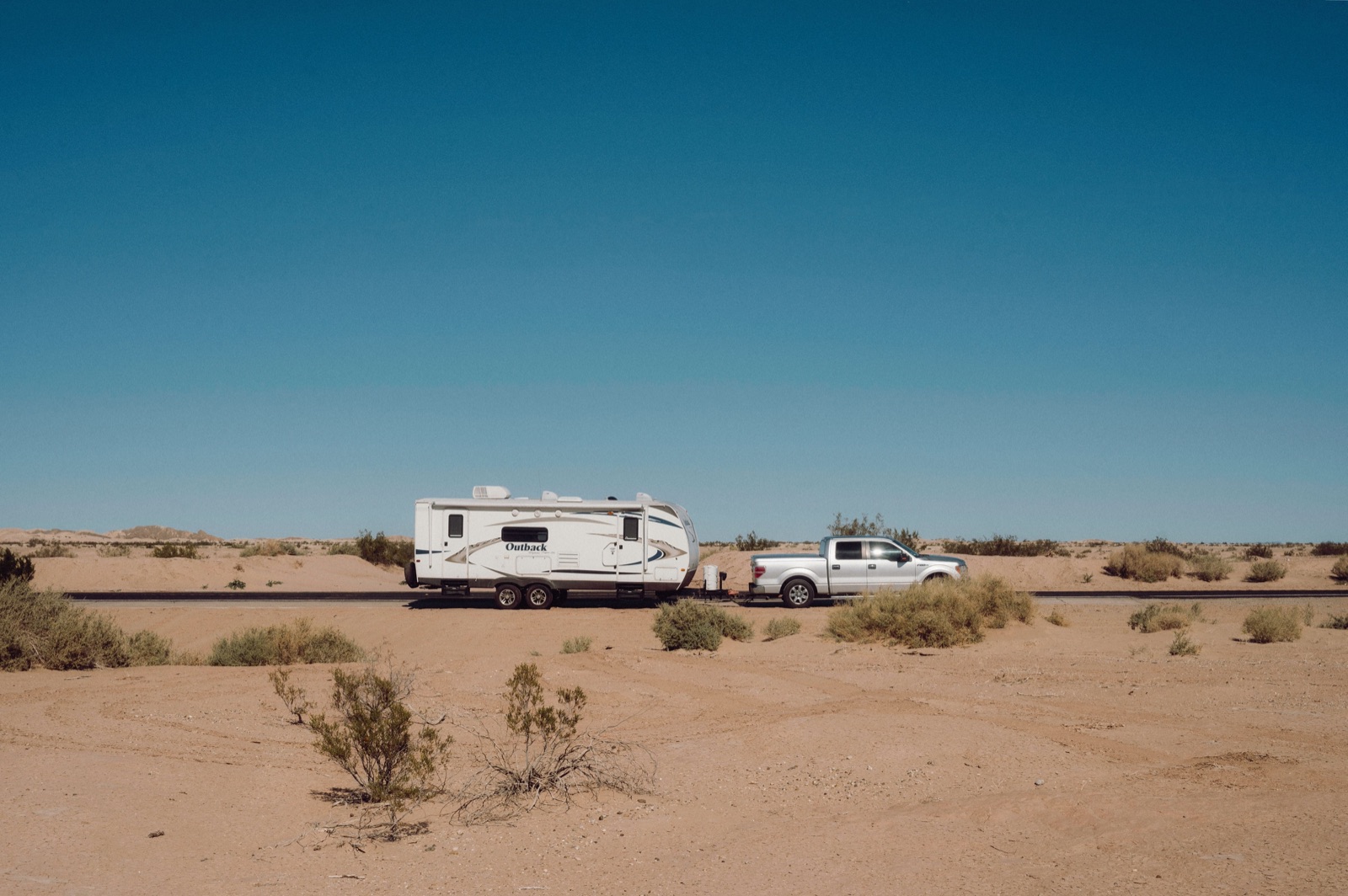 A pickup towing a travel trailer along a straight road through flat desert